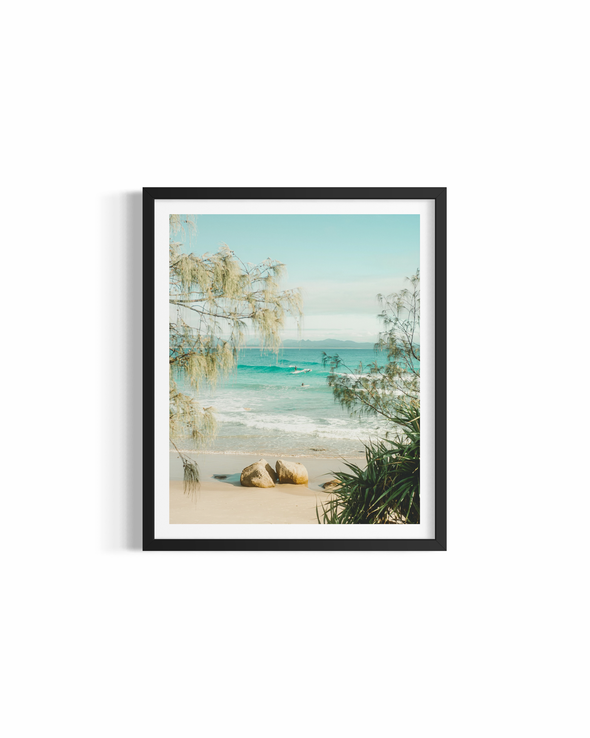 Lone surfer riding a wave at Wategos Beach framed by coastal trees — A Pocket of Paradise fine art print by Saxon Kent